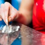 A hand using a card to prepare a line of white powder on a reflective surface