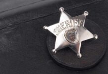 Badge Turned Predator — Jury Stunned A silver sheriff badge resting on a black leather surface