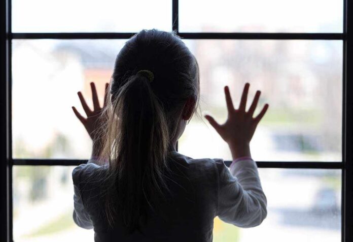 Young,Girl,At,Window,(in,Partial,Silhouette),Hands,Pressed,Against A child with long hair presses their hands against a window, looking outside