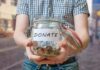 Hate Watchdog Indicted — Money Trail Stuns Person holding a glass jar labeled 'DONATE' filled with coins