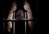 Architect Confesses To Killing Eight — Chills Courtroom Hands gripping prison bars in a dark setting