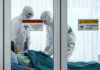 Ebola Explodes Amid Gunfire Healthcare workers in protective gear in quarantine room.