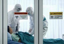Ebola Explodes Amid Gunfire Healthcare workers in protective gear in quarantine room.