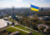 Winter Panic: Energy Boss Takes Power Large Ukraine flag with cityscape in background.