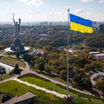 Winter Panic: Energy Boss Takes Power Large Ukraine flag with cityscape in background.