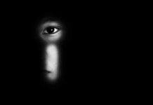 face peering through a keyhole in darkness