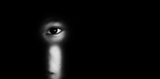 face peering through a keyhole in darkness
