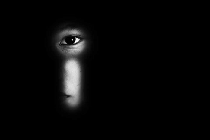 shutterstock_1304372611 face peering through a keyhole in darkness