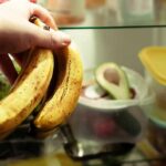 Hand holding two ripe bananas in a refrigerator