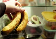 Hand holding two ripe bananas in a refrigerator