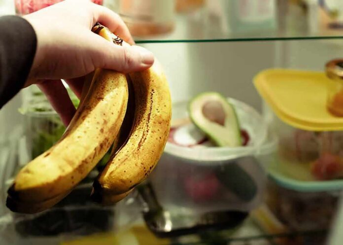 Hand holding two ripe bananas in a refrigerator