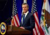 Governor Backtracks, Picks Rogan Fight Man in suit speaking at a podium with American and California flags