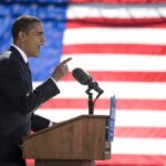 Speaker at podium with microphones in front of US flag