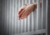handcuffed hands resting through prison bars
