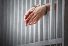 handcuffed hands resting through prison bars