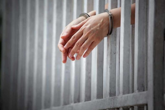 handcuffed hands resting through prison bars