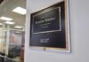 Office door plaque with gold trim outside a glass-walled conference room
