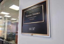 Affair Bombshell Entangles Ex-Senator Office door plaque with gold trim outside a glass-walled conference room