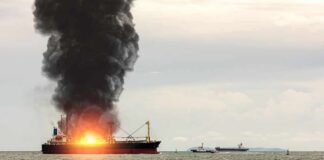 Cargo ship on fire with thick black smoke at sea