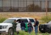 law enforcement officers confer beside patrol vehicles near a border fence