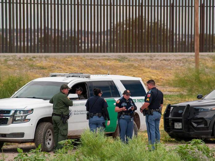 shutterstock_2015745392 law enforcement officers confer beside patrol vehicles near a border fence