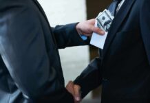Businessmen handshake as cash is slipped into a suit pocket