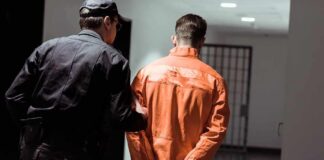 Police officer escorting handcuffed inmate in orange jumpsuit