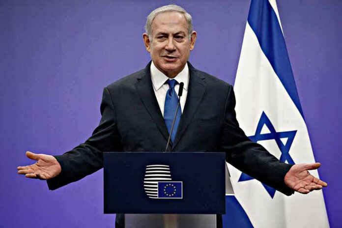 man in suit speaking at a podium with Israeli flag