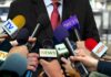 Press microphones surround a suited spokesperson