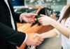 Hands exchanging car keys and a handshake at a dealership