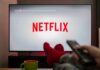 TV screen displaying Netflix with person holding remote