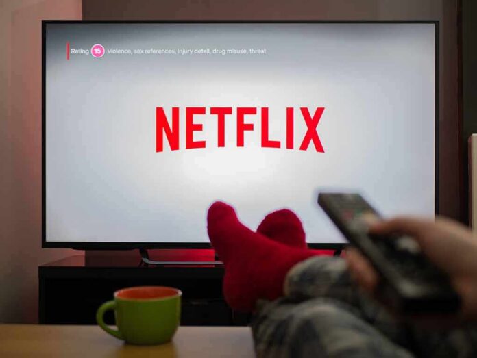 shutterstock_1683498799 TV screen displaying Netflix with person holding remote