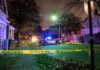 Police car blocks residential street at night behind caution tape