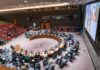 Delegates seated around a circular conference table in a large chamber