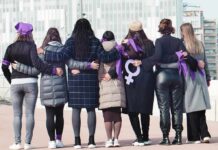 Bylaws Trump Identity – For Now Group of women standing arm in arm with purple ribbons