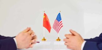 Two diplomats sit across table with China and United States flags between them
