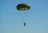Parachutist descending under a green round canopy