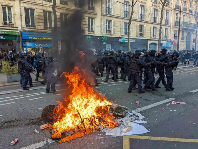 2261352259-1 Fire burning on the street amid police presence.