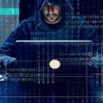 FBI Blitz Cracks Mega Scam Hubs Person in hoodie using a laptop with binary code overlay