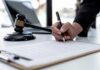 Shock Collar Torture Alleged In Manhattan Hand signing legal document beside gavel and laptop