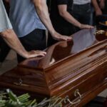 Mourners with hands on a polished wooden casket