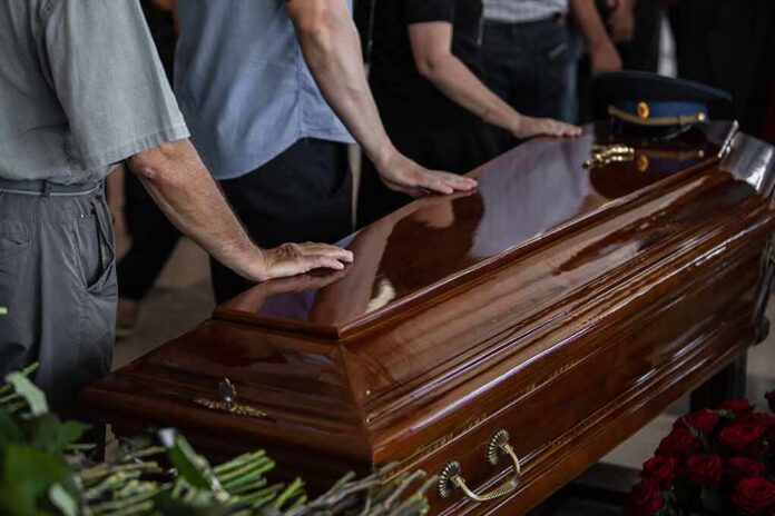 shutterstock_2122569467 Mourners with hands on a polished wooden casket
