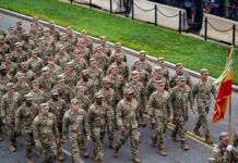 Soldiers in camouflage uniforms march in formation on a street