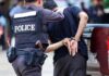 Weed Whacker Showdown Stops Knife-Wielding Attacker Police officer escorting a handcuffed man to a vehicle